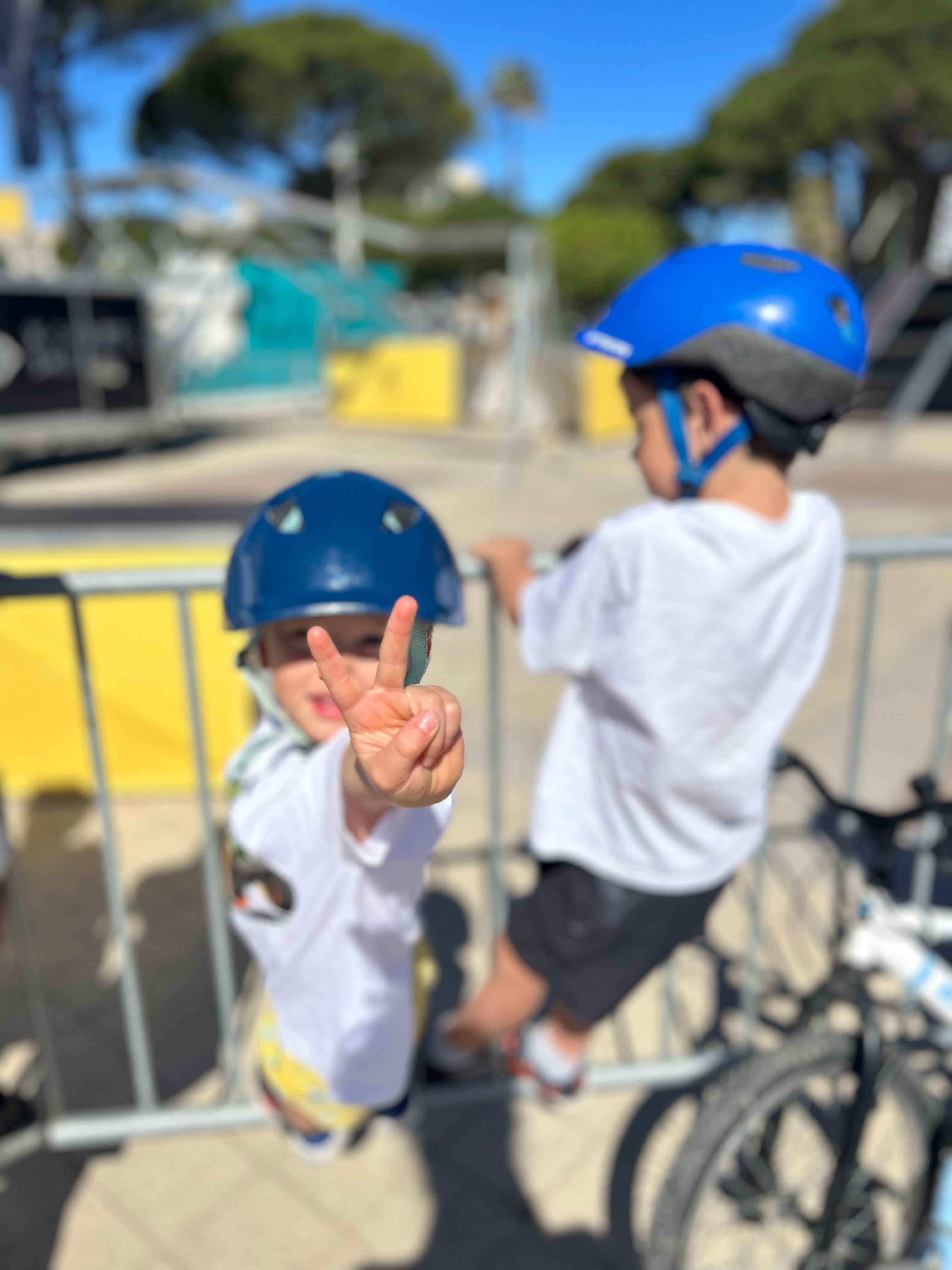 Dos niños con casco azul en un skatepark, junto a la valla y a su bicicleta