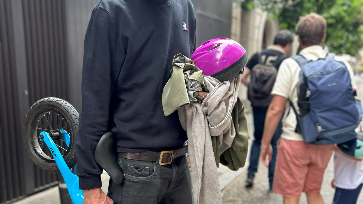 Un père porte à la main le vélo sans pédales de son enfant, le casque et les vêtements dans la rue